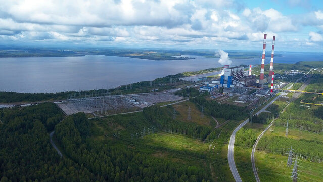 Top view of power plant on lake shore. Clip. Factory pipes on background of lake and green forest. Landscape with power station and pipes by lake in summer