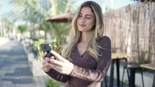 Young blonde woman smiling confident using smartphone at coffee shop terrace