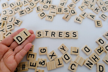 female hand closeup holds wooden alphabet blocks on background, changes word stress to distress,...
