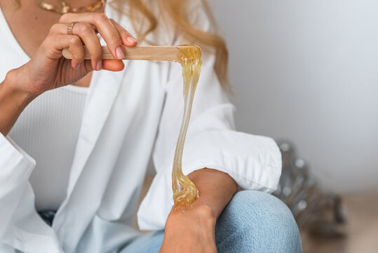 The hands of the beautician hold liquid sugar paste or wax for the duration of the depilation procedure in the salon. Close up, background image