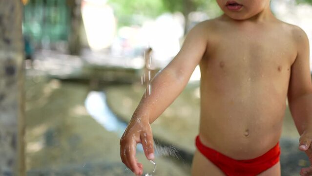 Little boy washing hands and arms outside during heat day. Refreshing water during summer day. Child wearing bathing suit brief