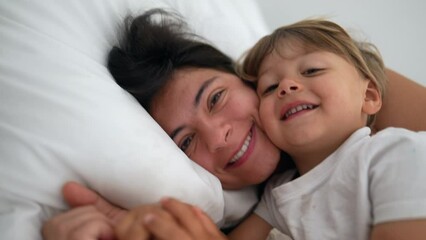 Mother and child son laying in bed together in authentic real life lifestyle moment. Motherhood love and affection with child in morning weekend