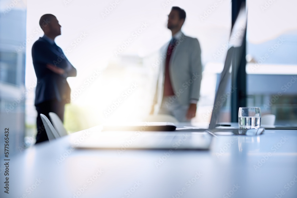 Poster big talk in the boardroom. shot of an open laptop on a boardroom desk with two businessmen blurred i
