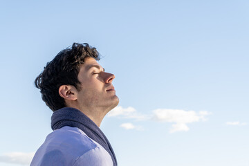 Young curly haired boy isolated on background of clear sky and with closed eyes smelling blue sky