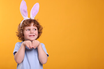 Obraz na płótnie Canvas Happy boy wearing cute bunny ears headband on orange background, space for text. Easter celebration