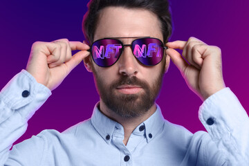 Confident man on color background. Abbreviation NFT reflecting in sunglasses - obrazy, fototapety, plakaty