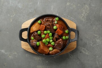 Delicious beef stew with carrots, peas and potatoes on grey table, top view