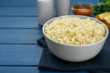 Bowl of tasty couscous on blue wooden table, closeup. Space for text