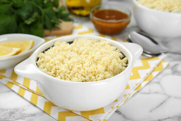 Bowl of tasty couscous on white marble table, closeup