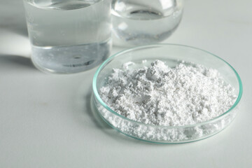 Petri dish with calcium carbonate powder and laboratory glassware on white table