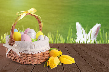 Bunny hiding in green grass near wooden deck with wicker basket full of Easter eggs