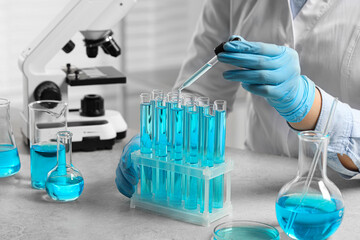 Fototapeta premium Scientist dripping liquid from pipette into test tube at white table in laboratory, closeup