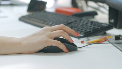 Close-up of woman working at computer in office. Creative. Woman drives computer mouse at desk. Woman's hand with manicure howls with computer mouse