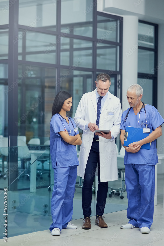 Canvas Prints Comparing diagnosis. Shot of a group of doctors talking together over a digital tablet while standing in a hospital.