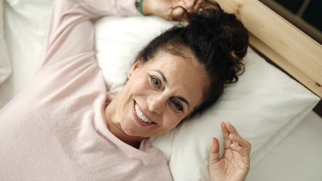 Middle age hispanic woman smiling confident lying on bed at bedroom