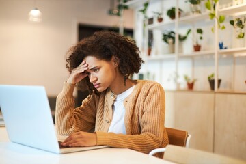 Concentrated multitasking young African American pretty woman working remotely on laptop