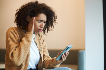 Stupefied African American woman expressing shock and astonishment while checking her mobile phone