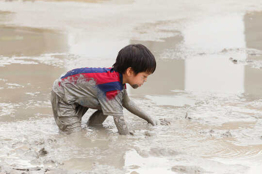cute happy asian little boy enjoying to play in the mud at playground. child learning in nature at montessori school. nature and education concept.
