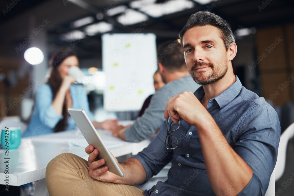 Poster Bringing digital ideas to the meeting. Portrait of a man sitting at a table in an office using a digital tablet with colleagues working in the background.
