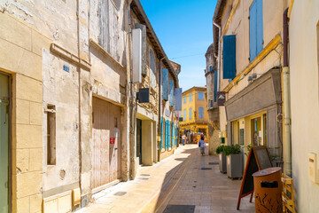 A woman walks down a narrow alley of shops  and apartments through the historic medieval town of Saint-Remy de Provence, France, on a sunny summer day in the Provence, Cote d'Azur region.
