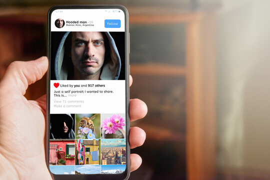 Man holding mobile phone with social media app interface on the screen, showing profile of young adult influencer man with photo shared by him as well as his gallery, likes and follow button. - Powered by Adobe