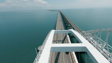 A long bridge for vehicles to cross the ocean. Drone view. Shot. A beautiful panorama overlooking the sunny clear sky and cars moving over a huge clear pond. © Media Whale Stock