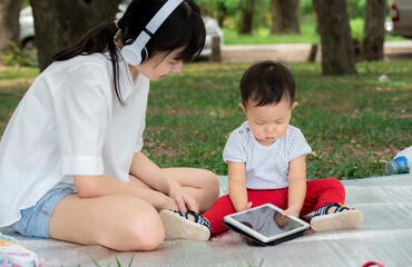 Beautiful young mother and baby listening to music in the park, Child in headphones is listening music from tablet