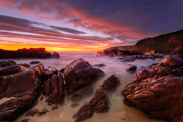 Vivid red sunrise over rocky beach coast - 577606450