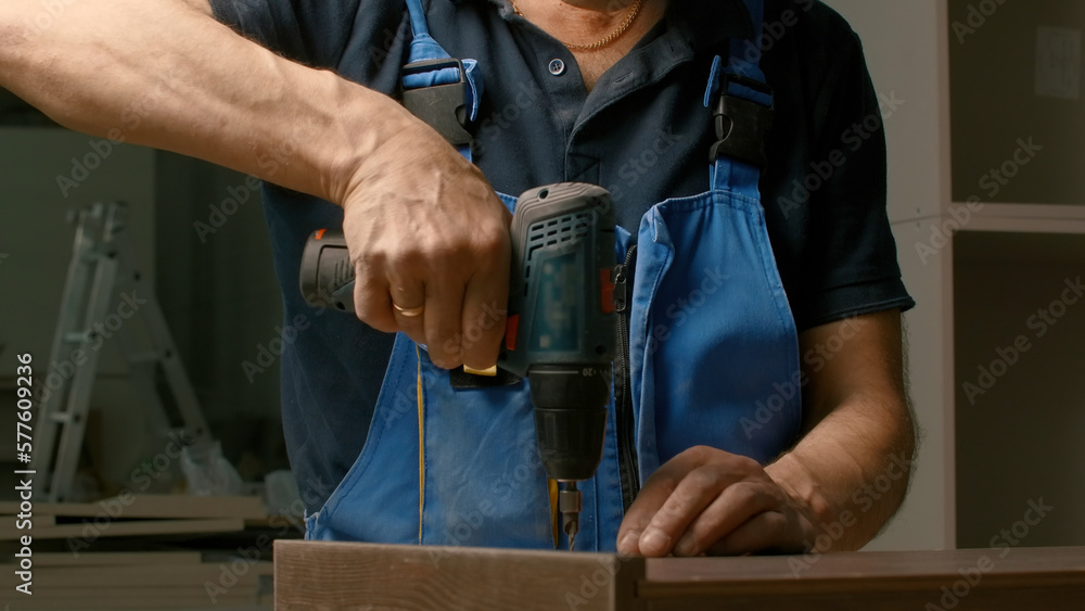 Poster close up of a man carpenter using screwdriver while working with a wooden product. creative. woodwor
