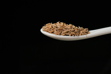 Dried cumin spice seeds on a spoon isolated on a black background. Dry seasoning in spoon. Spices and herbs for cooking zira