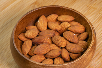 Almond nuts in wooden bowl on wooden background close up. Product rich in minerals and vitamins. Almond kernels. Healthy skin and hair and natural healing oil treatment