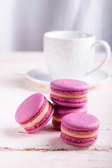 three pink macaroons and a white cup of coffee on a wooden table