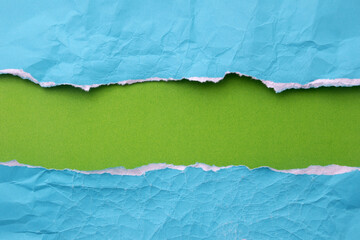 Torn creased blue paper laying over green paper background for text.