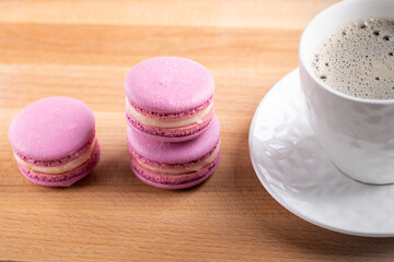 three pink macaroons and a white cup of coffee on a wooden table
