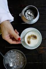 Flat lay top view of a woman hand holding a cup of creamy salted dripping Vietnamese coffee with ice bowl                               
