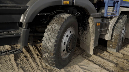 Close up of wheels of a slowly moving truck on sandy surface. Scene. Construction site background.