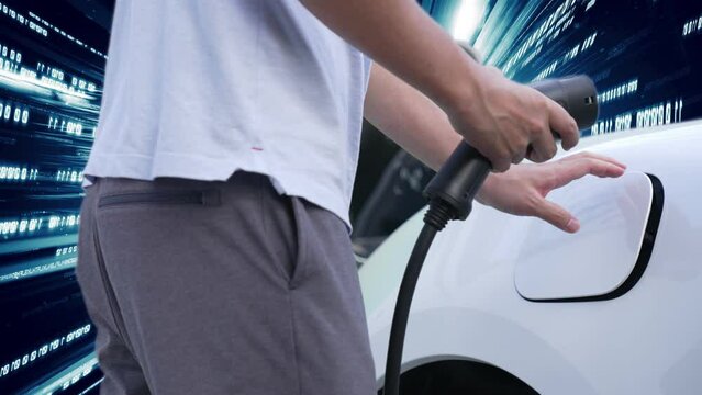 Progressive man charge electric car with power cable plug from charging station with technology background of binary code flying through votex. EV car concept with modern technology.