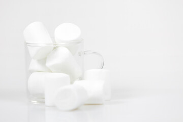 Marshmallows in a clear glass cup. white background. Focus on glass cup with marshmallows