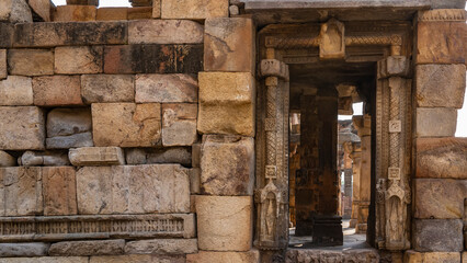 Ruins of an ancient temple in the Qutb Minar complex. Weathered brick sandstone walls are visible. The doorway is decorated with carvings. At the back of the hall is a colonnade. India. Delhi.