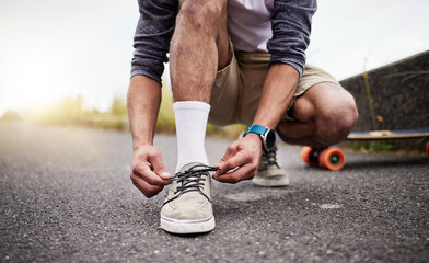 Hands, shoes and skate with a man tying his laces while on an asphalt skateboard for fun or...