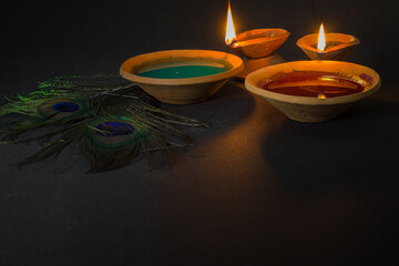 happy holi celebration with colors, clay lamp and peacock feather symbolizing hindu god krishna....