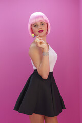 girl in the image of a doll on a pink background playfully licks a candy