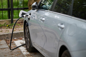 Naklejka premium Charging an electric car with a plug connected to the car at a charging station.