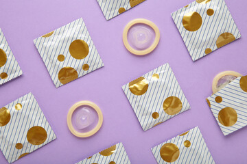 Opened condom and condom in pack on purple background. A condom use to reduce the probability of...