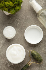 Face massage roller with cosmetic cream on grey background. Vertical photo