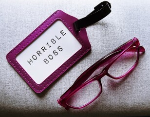 Purple reading glasses and ID card with text HORRIBLE BOSS, means supervisor who make workplace...
