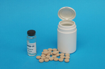 Plastic bottle, pills, ampoule with covid-19 vaccine on a blue background.