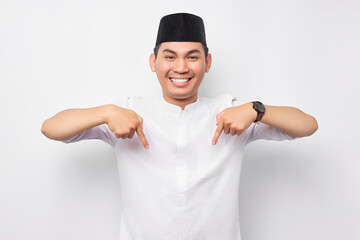 Cheerful handsome young Asian Muslim man wearing Arabic costume pointing finger at free space place...