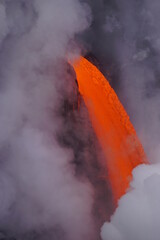 Lava flows down from high cliff into the ocean  surrounded by white steam, Big Island in Hawaii