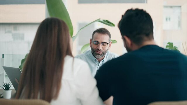 Video of real-estate agent showing house plans on electronic tablet while talking to the couple about buying the house in the office.